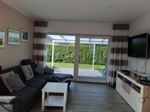 Uma sala de estar com sofá, mesa de centro, televisão e porta de vidro deslizante para um jardim.