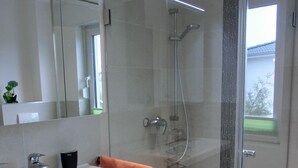 Un baño moderno con cabina de ducha de vidrio, lavabo blanco con tocador de madera y un espejo grande.