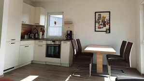 Una cocina moderna con armarios blancos, una mesa de comedor con cuatro sillas, una cafetera y una ventana con cortina.