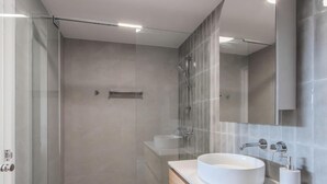Une salle de bain moderne avec une douche à parois de verre, un lavabo rond blanc et un meuble-lavabo en bois.