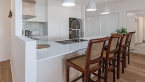 Une cuisine moderne avec des meubles blancs, un îlot central doté d’un évier et des luminaires suspendus.