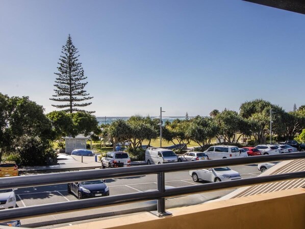 A parking lot with several cars, a large tree, and a view of the ocean. - Beachfront Apartment in Kingscliff (Kingscliff)