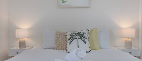 A neatly made bed with a folded towel, two bedside lamps, and a framed artwork of birds on the wall.