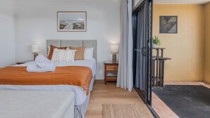 Une chambre d’hôtel avec un lit, des tables de chevet, une lampe, un tableau, une porte coulissante et une petite table avec une plante.