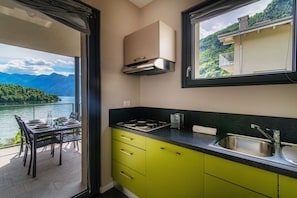 A kitchen with a view of a lake and mountains, a dining area with a table set for two, and a window with a balcony.