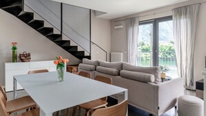 A modern living space with a dining area, sofa, staircase, and large windows with a view. - Lake's Dream - MyHomeinComo (Ossuccio)