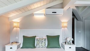 A bedroom with a sloped ceiling, white walls, a bed with green pillows, bedside lamps, and an air conditioning unit. - Lake's Dream - MyHomeinComo (Ossuccio)