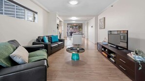 A living room with a sofa, a coffee table, a TV, and a kitchen in the background. - Superb! 2Bed, 2Bath, 1Car, VIEWS ~ CBD (Brisbane City)