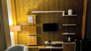 Ein modernes Wohnzimmer mit Flachbildfernseher, Holzpaneelen, eingebauten Regalen, einem grauen Sessel und einem Couchtisch.