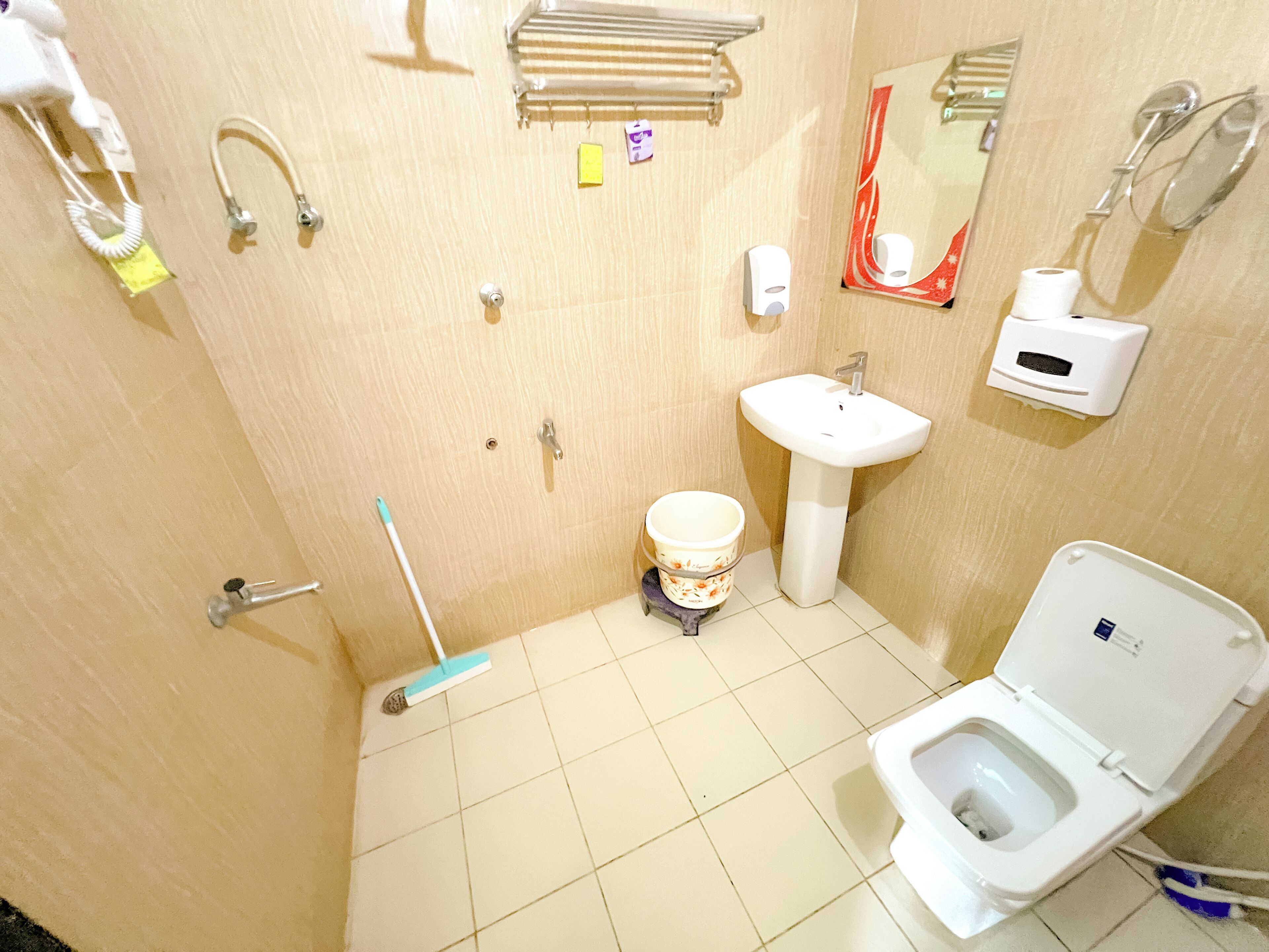 A bathroom with a toilet, sink, hand dryer, and a mop.