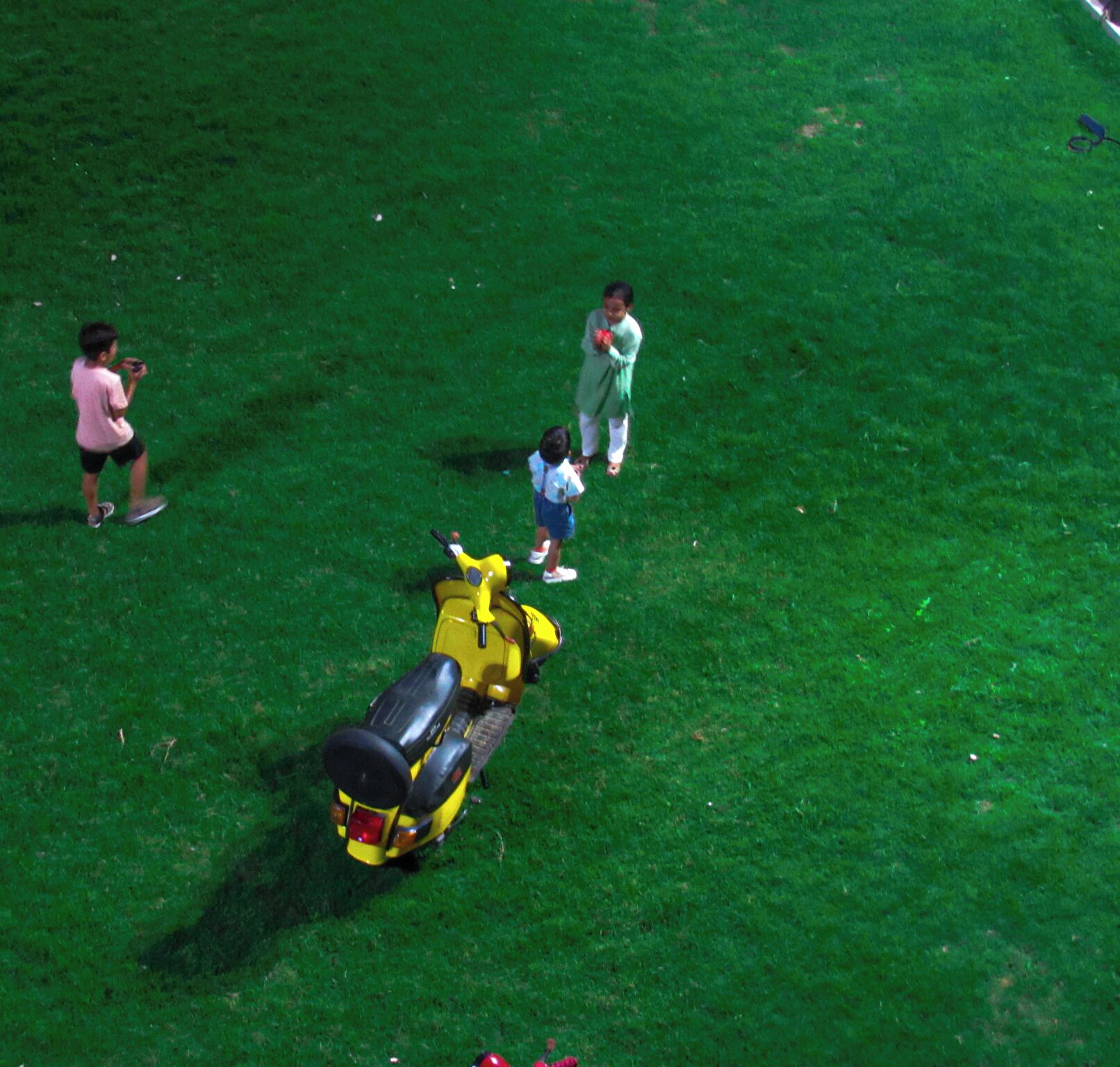 A green lawn with a yellow scooter and a child.