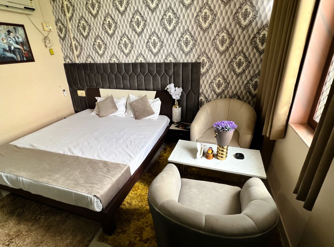 Una habitación de hotel con una cama grande, una cama más pequeña, un sofá, una mesita de noche y un florero con flores.