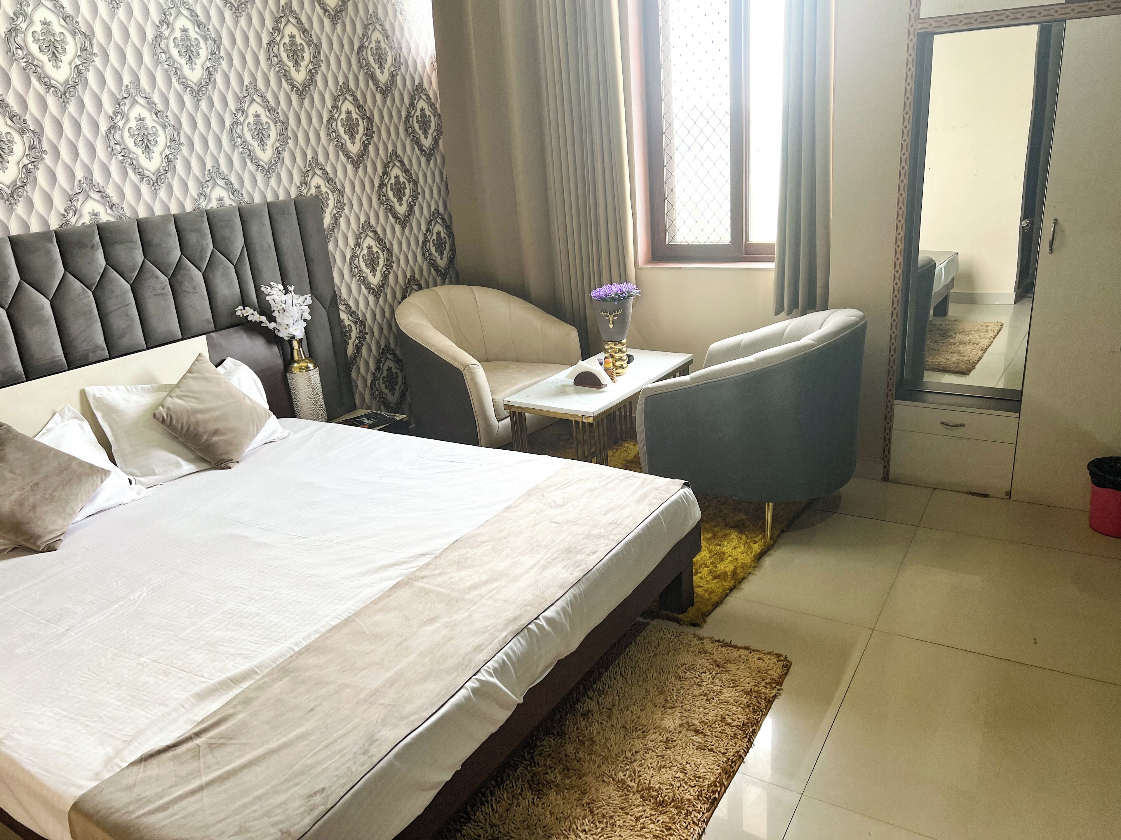 Una habitación de hotel con una cama, una silla, una mesita, una ventana con cortinas y una puerta.