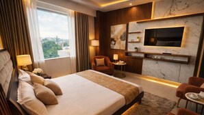 Ein Hotelzimmer mit einem großen Bett, einem an der Wand befestigten Fernseher, einer Sitzecke mit Sessel und Tisch und Blick ins Freie.