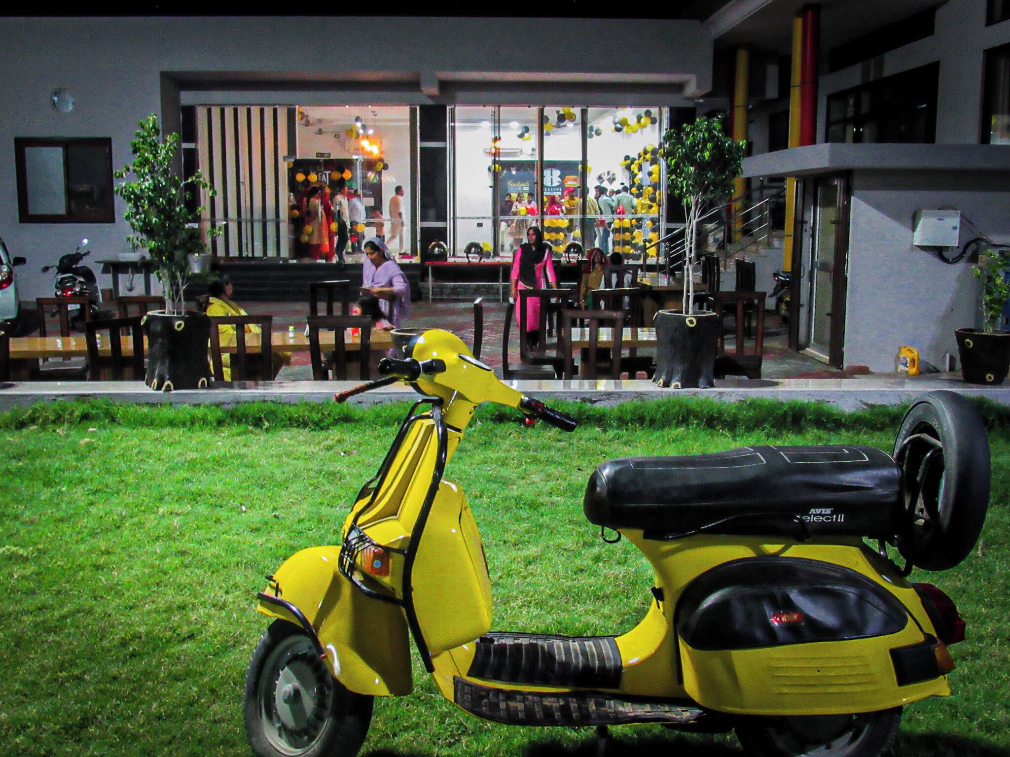 Un scooter jaune est garé sur l’herbe devant un immeuble qui abrite un restaurant.