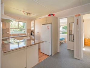 A compact kitchen with a refrigerator, a microwave, and a sink. There is a window providing natural light and a door leading to another room.