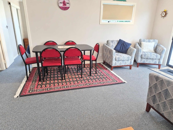A room with a dining table and chairs, two armchairs, a patterned rug, and a clock on the wall.