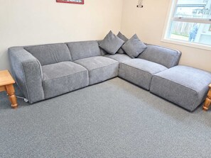 Ein graues Ecksofa mit einem Holztisch und einem Fenster mit Blick ins Freie.