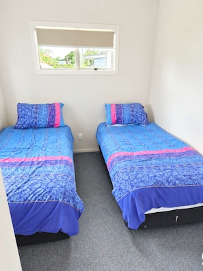 A small, clean room with two single beds, a window, and a carpeted floor.