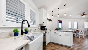 A kitchen with white cabinetry, a marble countertop, a sink, and a ceiling fan. - The Good Life · Ultimate Gulf Shores Getaway: Hot Tub, RV Pad, Fire-Pit & Beach (Gulf Shores)