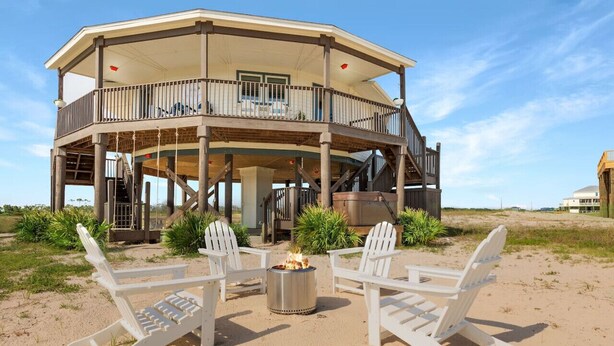 A beach house with a covered deck, outdoor seating, and a fire pit. - The Good Life · Ultimate Gulf Shores Getaway: Hot Tub, RV Pad, Fire-Pit & Beach (Gulf Shores)