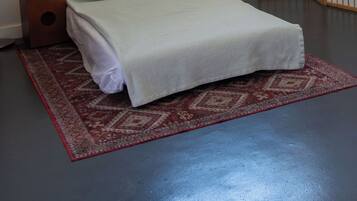 A bedroom with a bed, a bedside table with a tissue box, a red patterned rug, and a shoji screen.