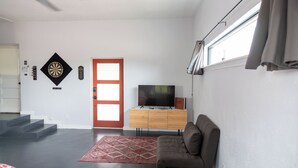 A modern living room with a sofa, a television on a wooden cabinet, a red patterned rug, and a dartboard on the wall. - La Cochera Private Apartment - No Cleaning Fee (Alpine)