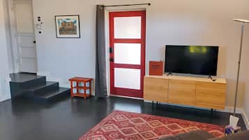 A living room with a TV, a red door, a staircase, and a patterned rug.