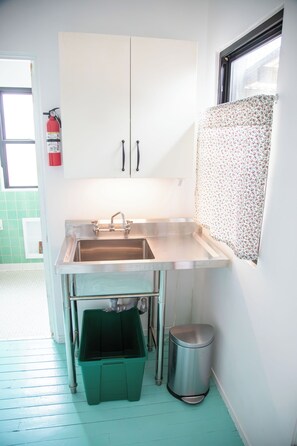 A kitchen with a stainless steel sink, a green trash bin, and a fire extinguisher mounted on the wall.