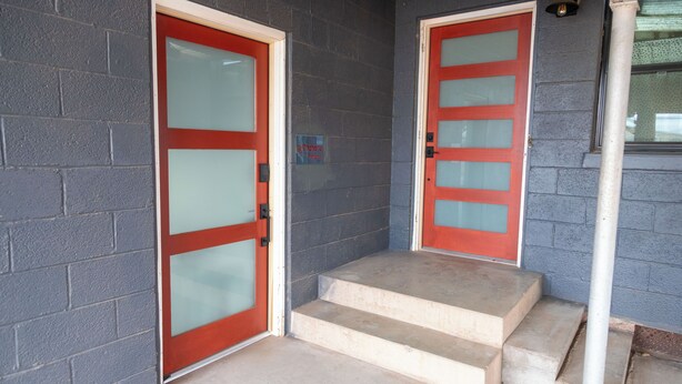 A building entrance with two red doors, a small sign above the left door, and a set of concrete steps leading up to the door. - La Cochera Private Apartment - No Cleaning Fee (Alpine)