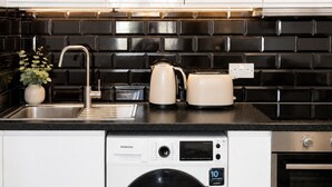 A compact kitchen with a washing machine, a toaster, and a kettle on the countertop. - Grand Central House - Deluxe Two Bedroom (Gibraltar)