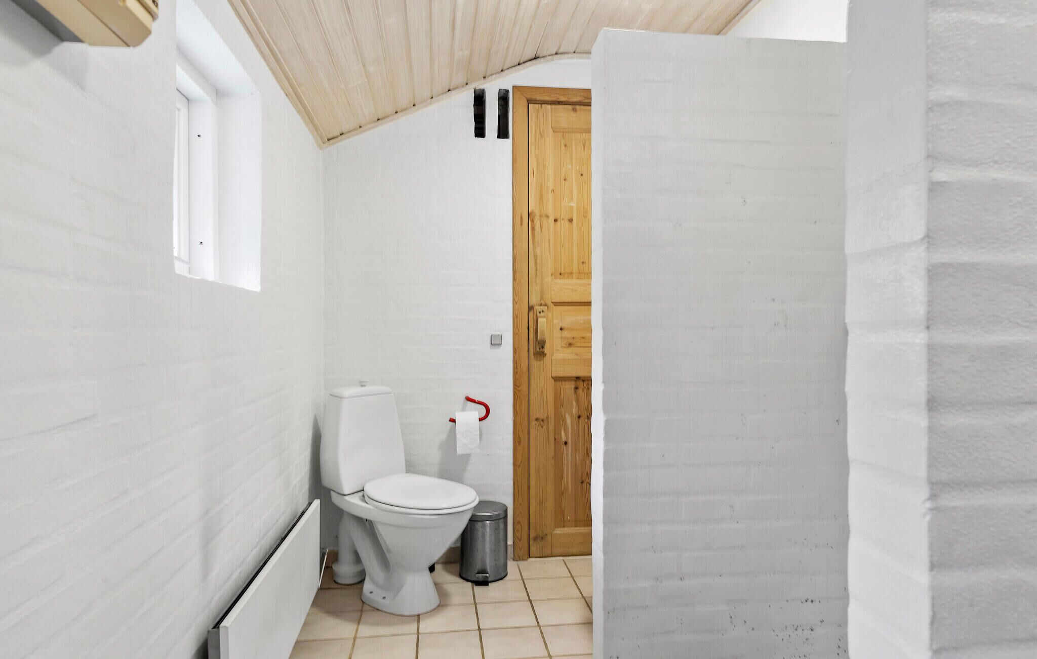 Ein kleines, schmales Badezimmer mit einer weißen Toilette, einer Holztür und einem kleinen Mülleimer.