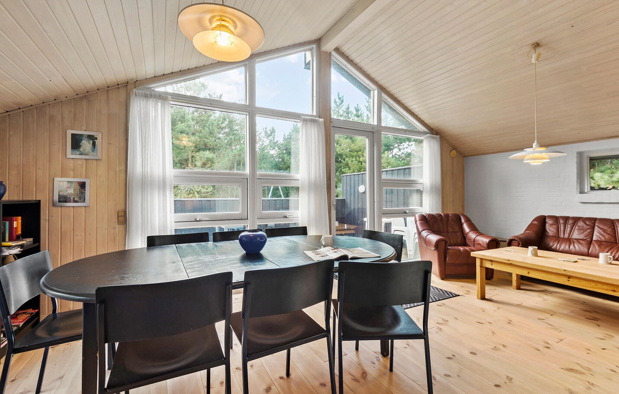 A spacious room with a large dining table, several chairs, a brown leather sofa, and a wooden bench.