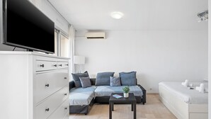 A modern, minimalist living room with a sofa, a flat-screen TV, a coffee table, and a white cabinet.