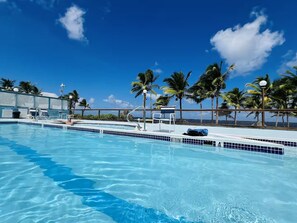 A clear blue pool with a 'NO DIVING' sign, surrounded by palm trees and a view of the ocean.
