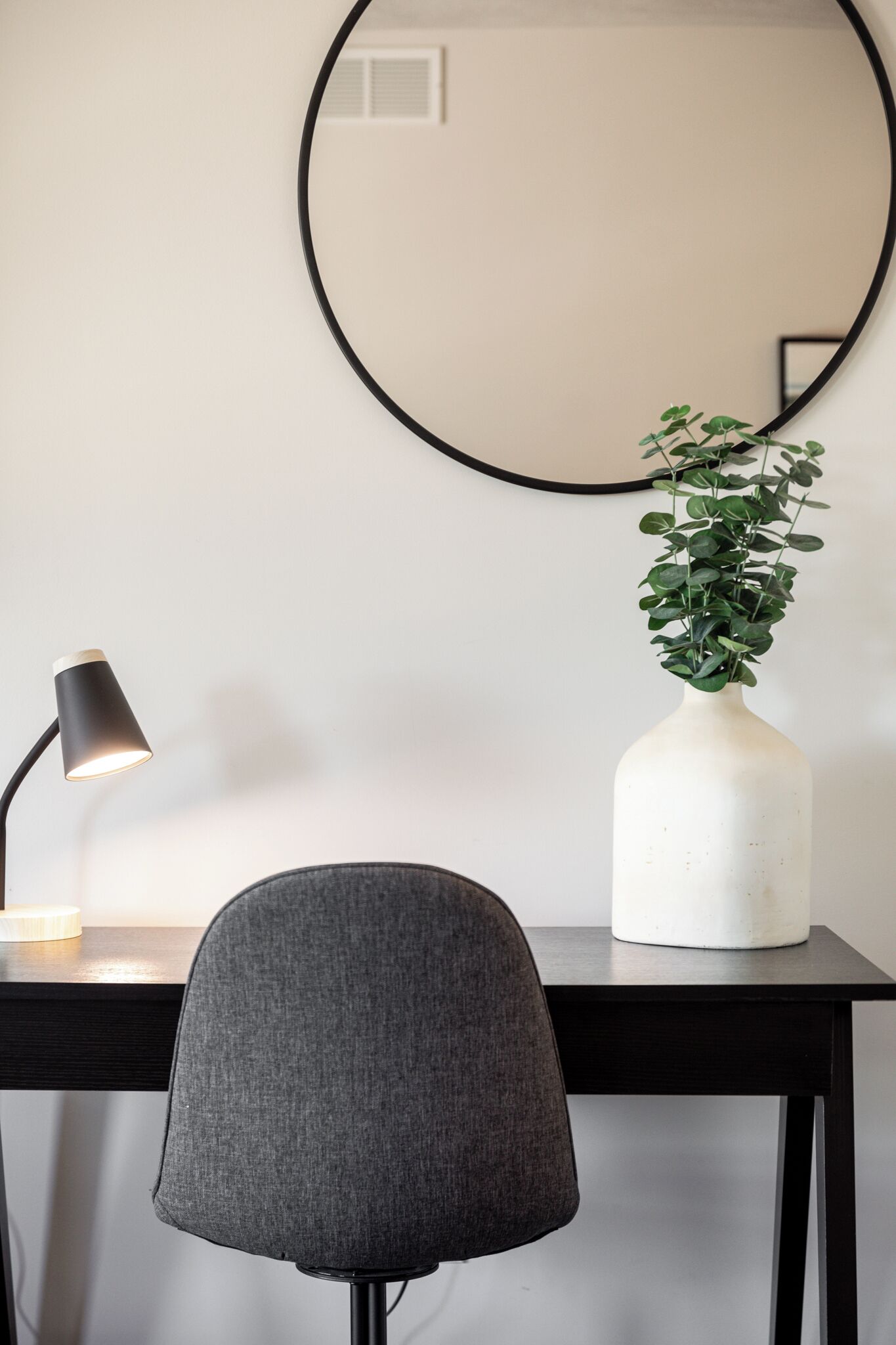 A desk with a lamp, a chair, and a vase with a plant.