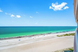 A beach view with clear turquoise water, a sandy shore, and a few umbrellas. - 🩱Luxurious CBC 1-18C: Beach Front Condo | Heated Pool | Gym | Pickleball | Sauna | Hot Tubs! (Clearwater Beach)