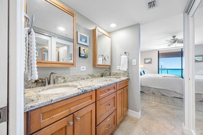 A bathroom with a granite countertop, wooden cabinets, and a large mirror. - 🩱Luxurious CBC 1-18C: Beach Front Condo | Heated Pool | Gym | Pickleball | Sauna | Hot Tubs! (Clearwater Beach)