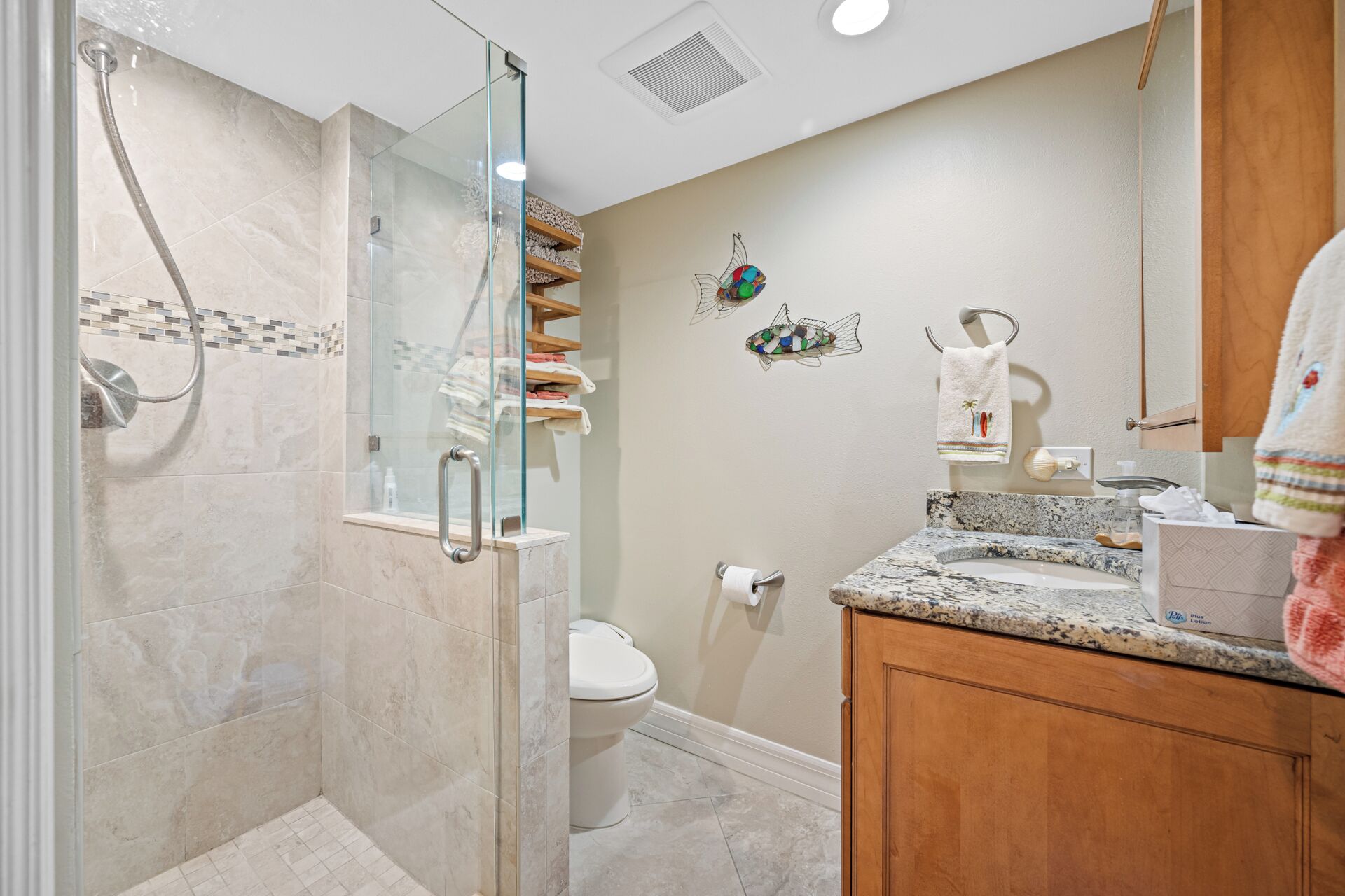 A bathroom with a glass shower enclosure, a toilet, a sink with a marble countertop, and wooden cabinets.