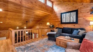 A cozy cabin interior with a wooden ceiling, a staircase, a living area with a sofa and coffee table, and a framed picture on the wall. - Legacy Lodge Cabin-Near Helen,GA Hot Tub,Screened deck, Tubing,Hiking,Loft (Sautee Nacoochee)