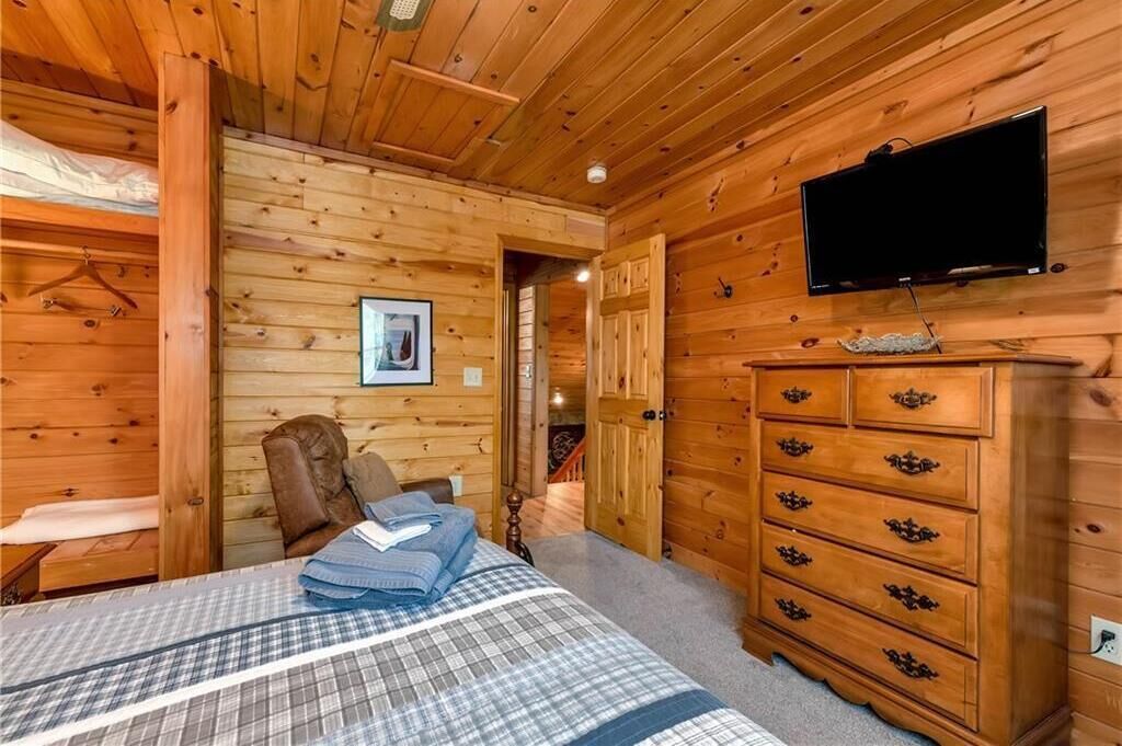 A wooden cabin room with a bed, a dresser, a television, and a picture on the wall.