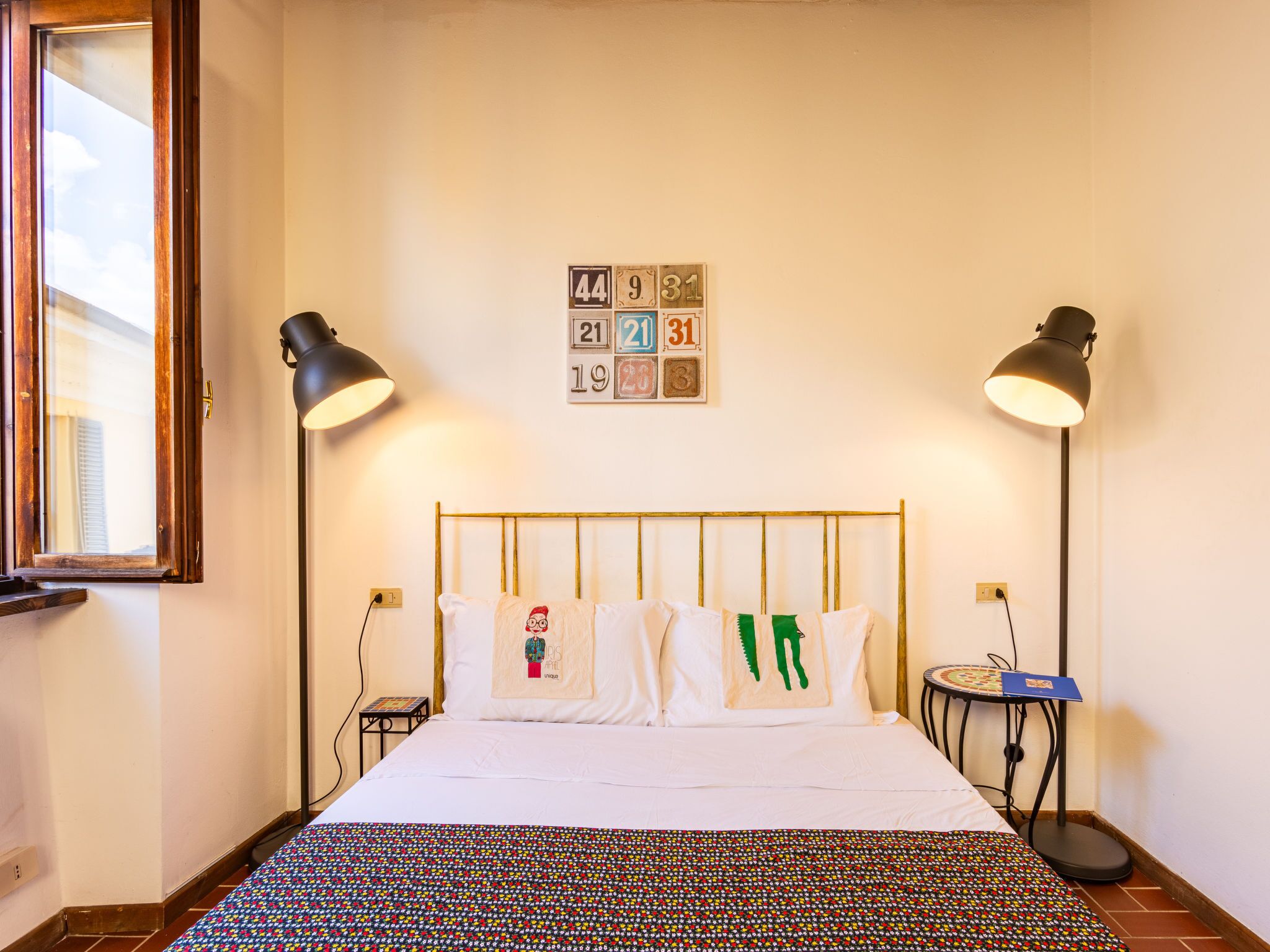 Ein ordentlich eingerichtetes Hotelzimmer mit einem Bett, zwei Nachttischlampen, einem kleinen Tisch und einem Wandkalender.