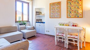 Un salon chaleureux avec un canapé, une table à manger et des chaises, une fenêtre ornée de plantes et deux œuvres d’art colorées accrochées au mur.