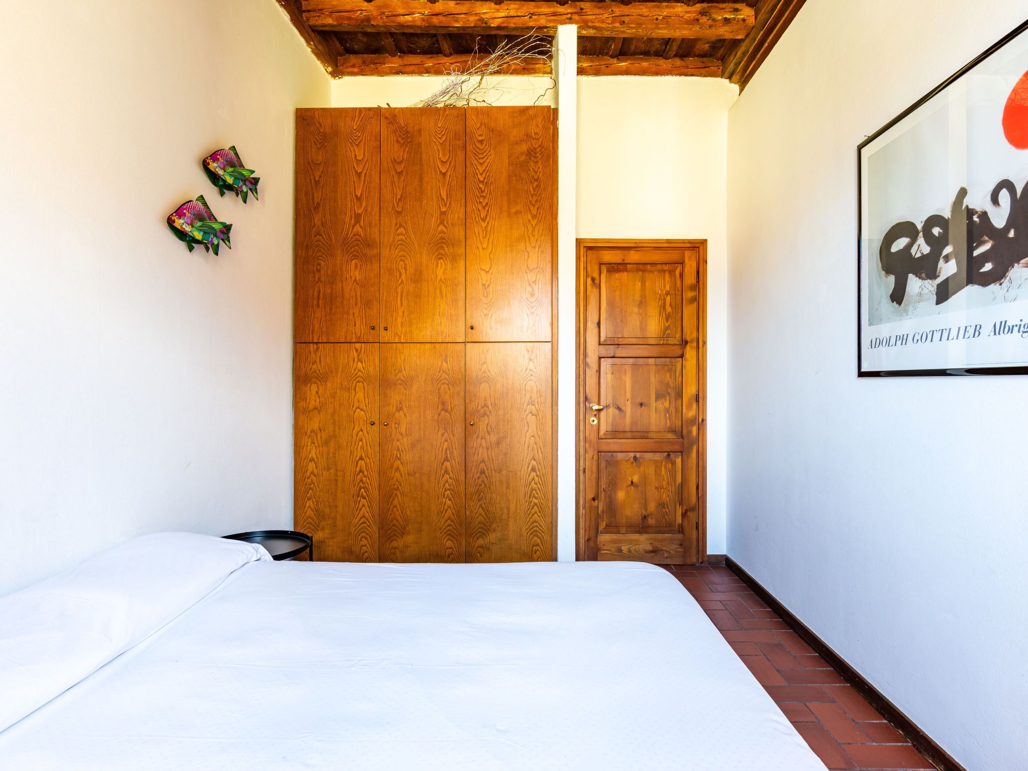 A bedroom with a wooden wardrobe, a bed, and a framed artwork on the wall.