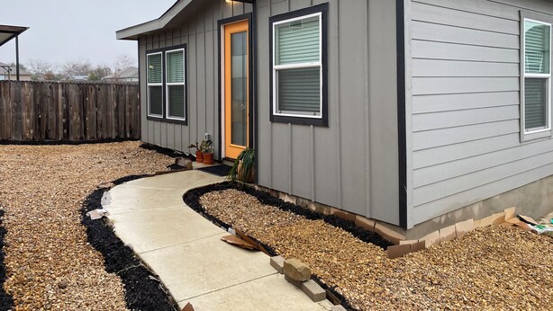 A residential building with a grey exterior, a concrete pathway, and a wooden fence in the background. - Frida's Tiny Home (San Antonio)