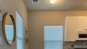 A living room with a black sofa, a white side table, and a small white cabinet. There is a large mirror on the wall, a potted plant, and a window with blinds. - Frida's Tiny Home (San Antonio)