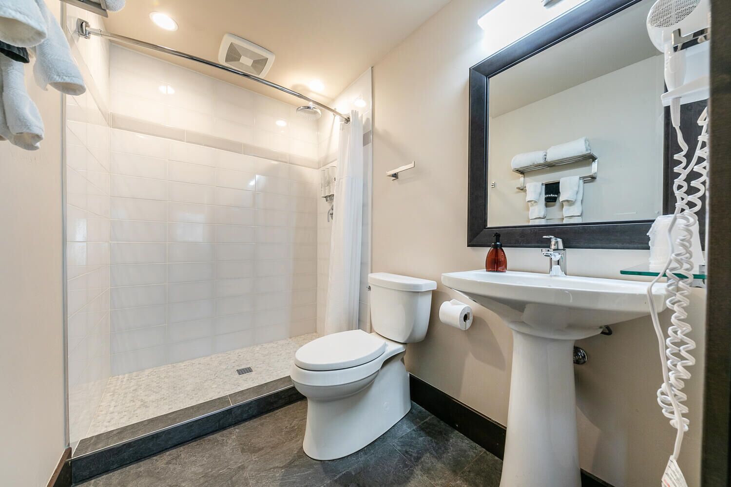 Une salle de bain moderne avec une douche à parois de verre, des toilettes blanches et un lavabo sur colonne avec un miroir au-dessus.