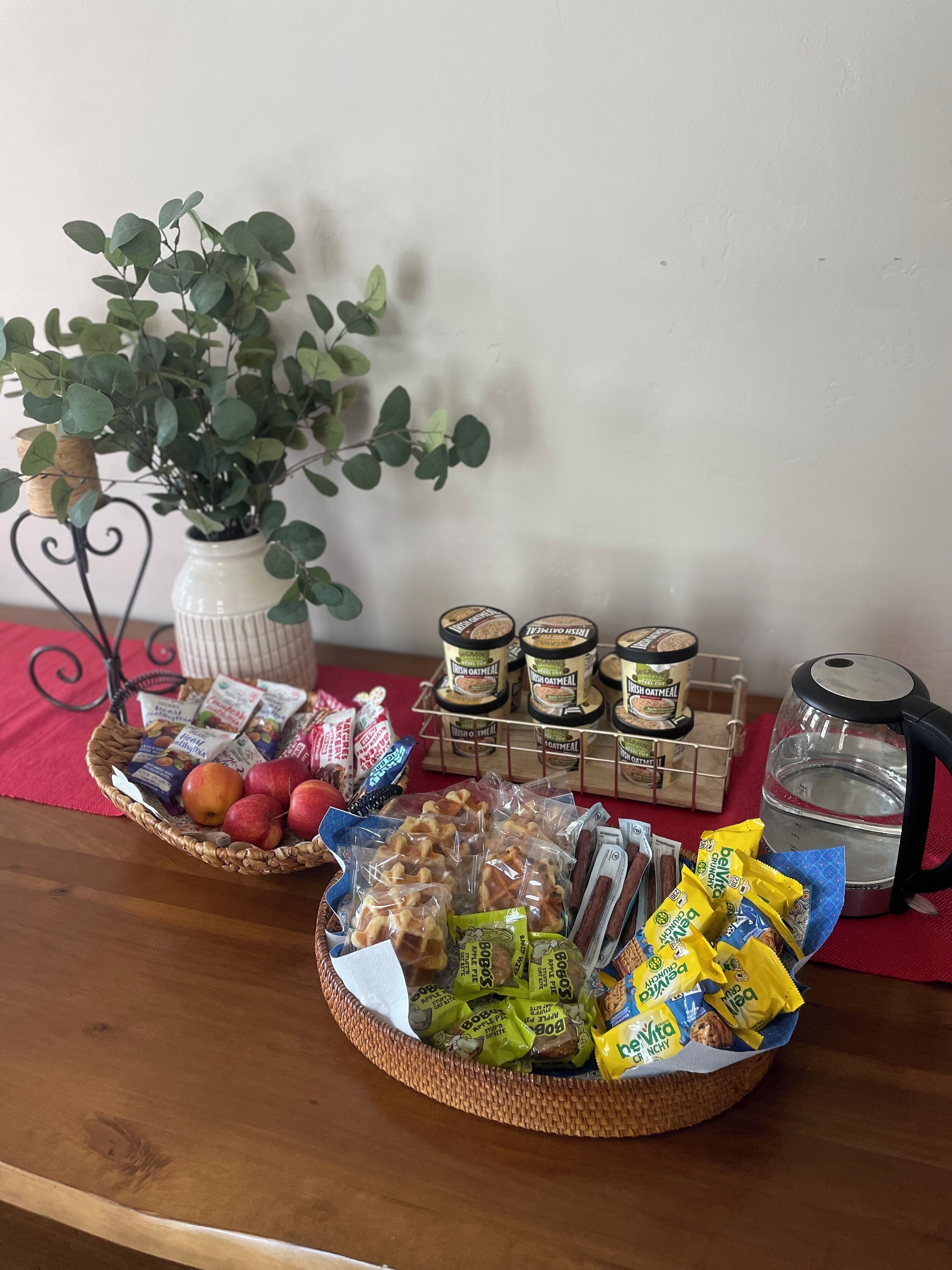 A table with various food items including jars of oatmeal, a basket of apples, and packets of bread.