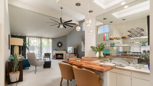 A spacious living area with a wooden dining table, two chairs, a fireplace, and a modern ceiling fan.