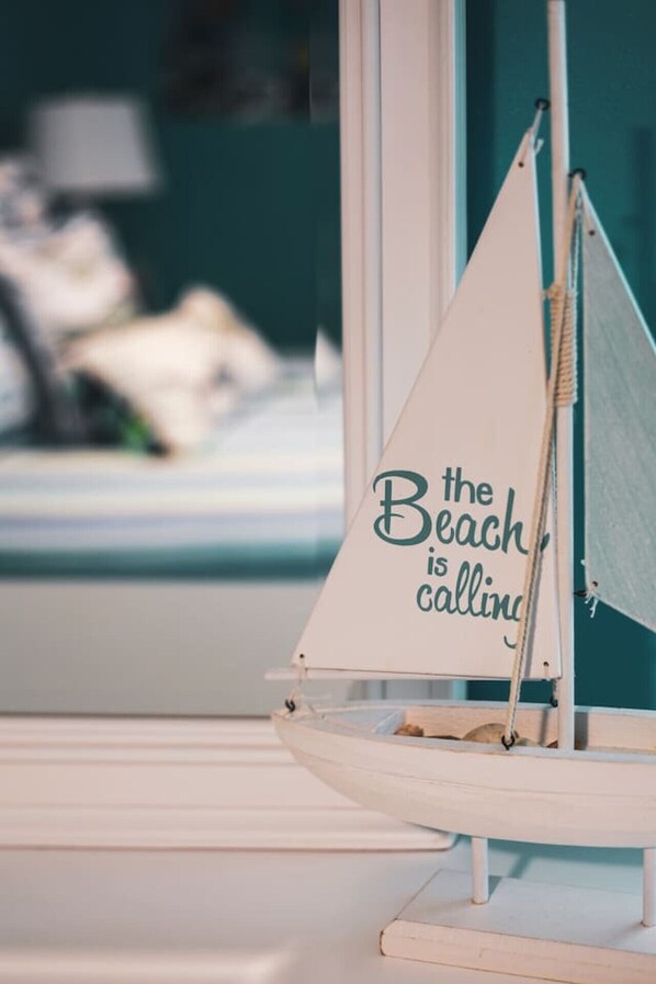 Ein Segelboot mit dem Aufdruck "the Beach is calling", platziert in der Nähe eines Fensters.